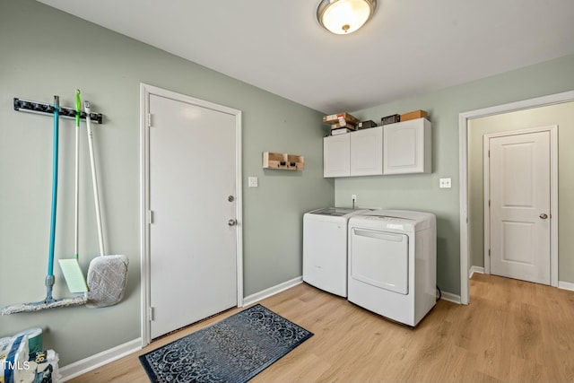 washroom featuring light wood-type flooring, washing machine and dryer, cabinet space, and baseboards