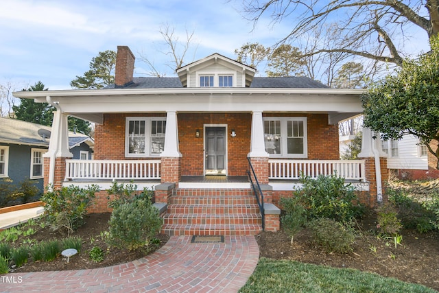 bungalow-style house featuring brick siding, a chimney, and a porch