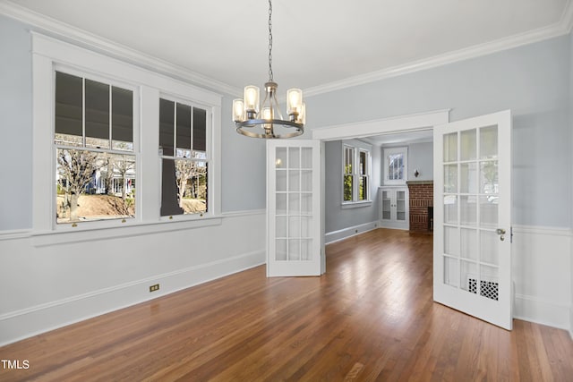 unfurnished dining area with french doors, an inviting chandelier, ornamental molding, wood finished floors, and baseboards