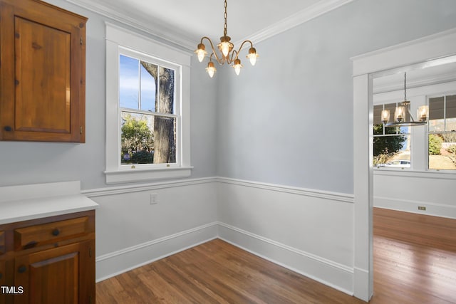 unfurnished dining area featuring a healthy amount of sunlight, ornamental molding, a notable chandelier, and wood finished floors