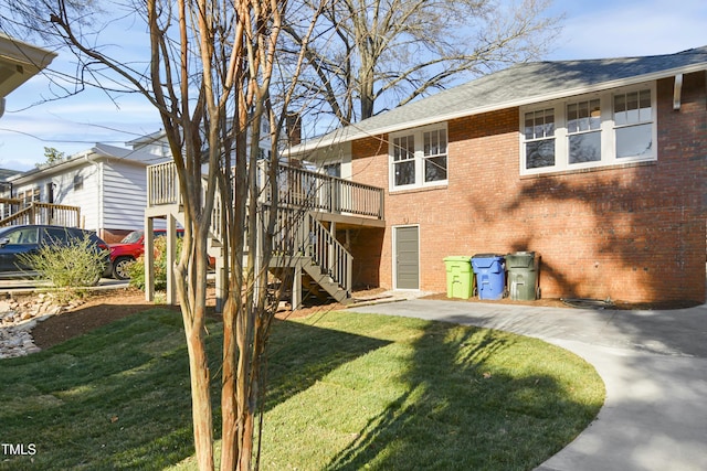 back of property featuring stairs, a yard, brick siding, and a deck