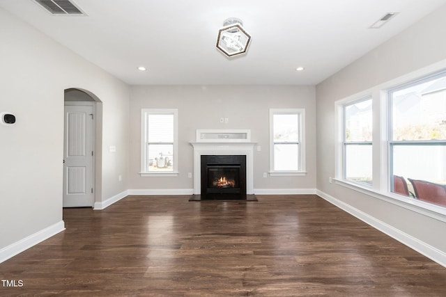 unfurnished living room with dark wood-style floors, arched walkways, visible vents, and baseboards