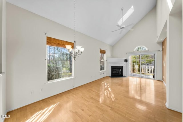 unfurnished living room with a fireplace with flush hearth, ceiling fan with notable chandelier, high vaulted ceiling, and wood finished floors