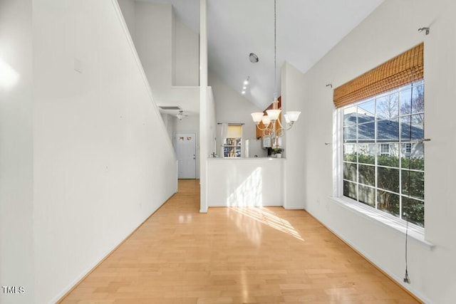 interior space featuring a chandelier, high vaulted ceiling, wood finished floors, and freestanding refrigerator