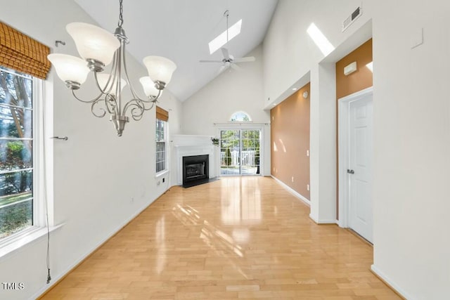 unfurnished living room with a skylight, light wood finished floors, visible vents, a fireplace with flush hearth, and high vaulted ceiling