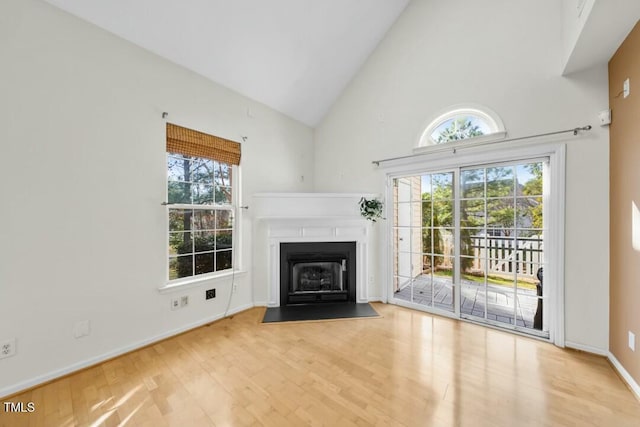 unfurnished living room featuring high vaulted ceiling, a fireplace with flush hearth, baseboards, and wood finished floors