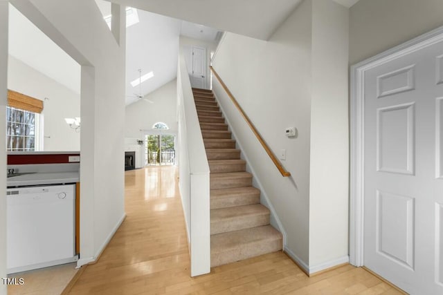 stairs with a skylight, a fireplace, a towering ceiling, wood finished floors, and baseboards