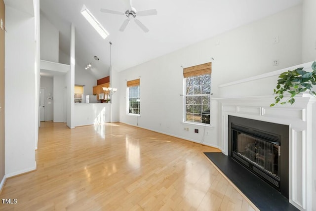 unfurnished living room with high vaulted ceiling, a glass covered fireplace, light wood-style flooring, and ceiling fan with notable chandelier