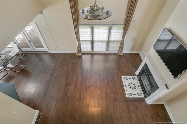 unfurnished living room with a notable chandelier, wood finished floors, visible vents, baseboards, and a glass covered fireplace