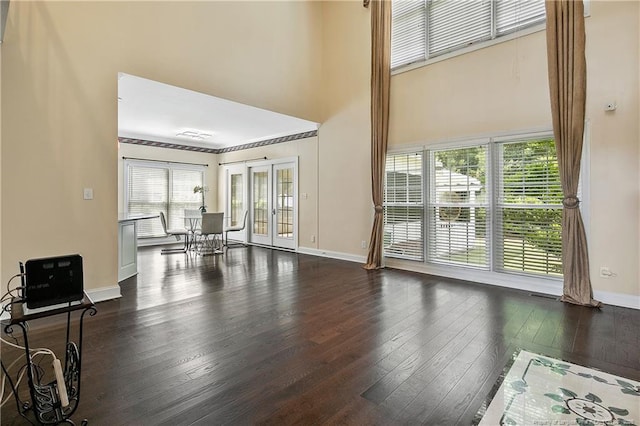 living area with french doors, a towering ceiling, hardwood / wood-style flooring, and baseboards