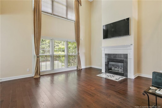 unfurnished living room featuring baseboards, a high ceiling, a tiled fireplace, and wood finished floors