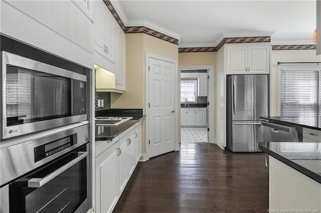 kitchen featuring dark wood-style floors, stainless steel appliances, ornamental molding, white cabinets, and a sink