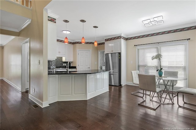 kitchen featuring a peninsula, dark wood-style flooring, ornamental molding, freestanding refrigerator, and dark countertops