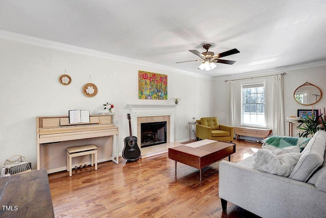 living area featuring a fireplace with raised hearth, a ceiling fan, wood finished floors, crown molding, and baseboards