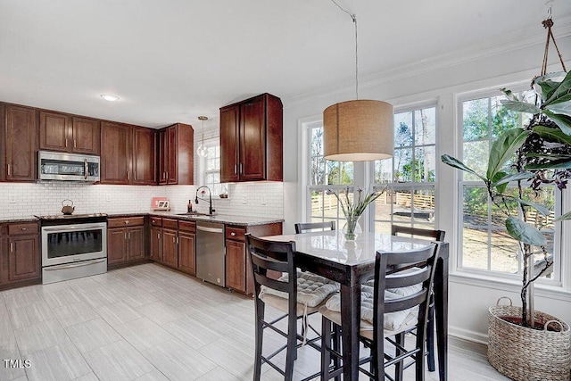 kitchen with backsplash, crown molding, pendant lighting, appliances with stainless steel finishes, and a sink