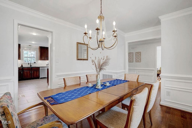 dining room featuring light wood-style flooring, ornamental molding, wainscoting, a decorative wall, and a chandelier