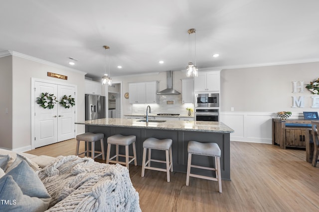 kitchen with appliances with stainless steel finishes, white cabinets, a sink, wall chimney range hood, and a kitchen breakfast bar