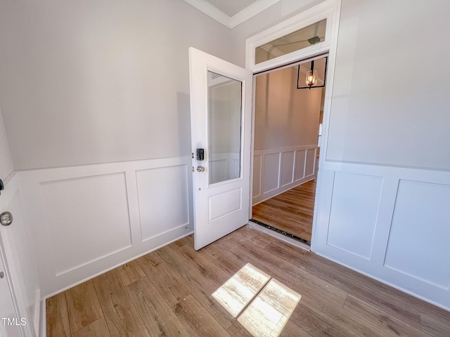 entryway with ornamental molding, a decorative wall, wood finished floors, and wainscoting