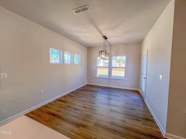 unfurnished dining area with dark wood-type flooring, a chandelier, visible vents, and baseboards