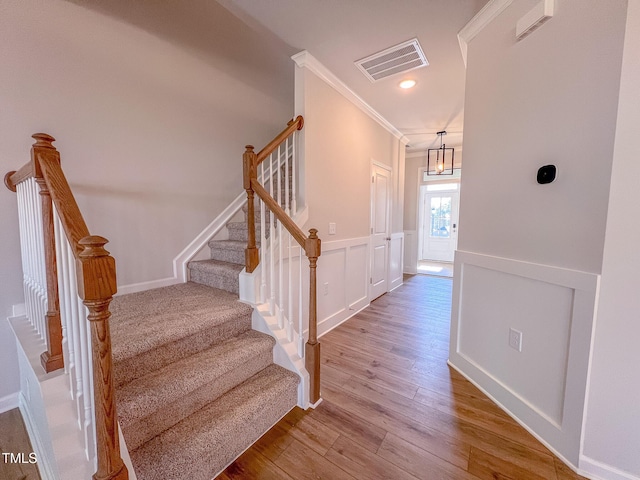 stairs featuring visible vents, wainscoting, ornamental molding, wood finished floors, and a decorative wall