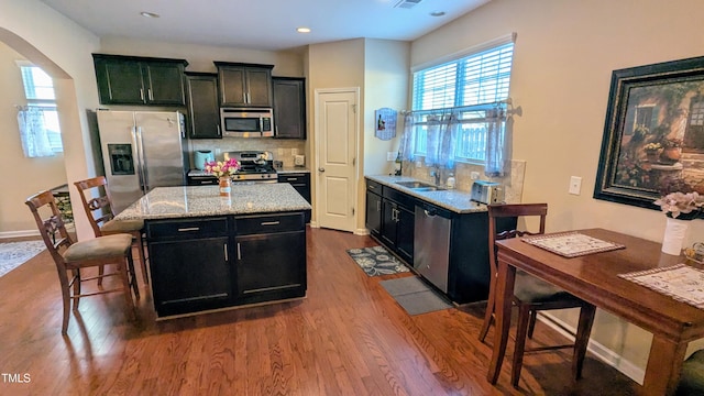 kitchen featuring arched walkways, a kitchen island, appliances with stainless steel finishes, dark wood-type flooring, and dark cabinets