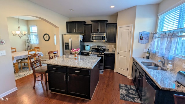 kitchen featuring arched walkways, dark wood finished floors, stainless steel appliances, a sink, and a kitchen island