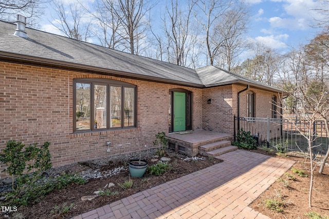 exterior space featuring roof with shingles, fence, and brick siding