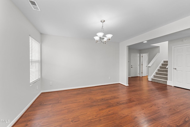 empty room featuring baseboards, stairway, wood finished floors, and a notable chandelier