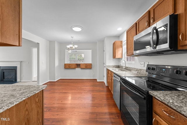 kitchen featuring dark wood-style flooring, a fireplace with flush hearth, a sink, appliances with stainless steel finishes, and brown cabinets