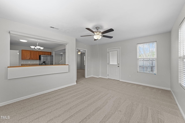 unfurnished living room featuring ceiling fan with notable chandelier, carpet, visible vents, and baseboards