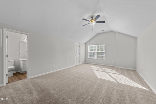 unfurnished bedroom featuring lofted ceiling, baseboards, ensuite bath, and carpet