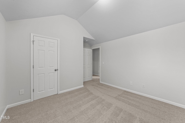 unfurnished bedroom with lofted ceiling, light carpet, and baseboards