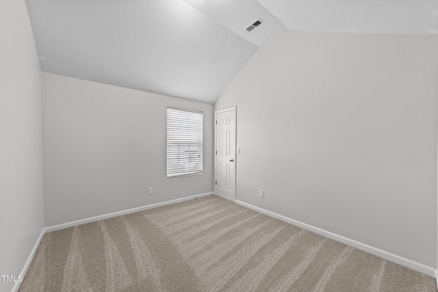 carpeted spare room with baseboards, visible vents, and vaulted ceiling