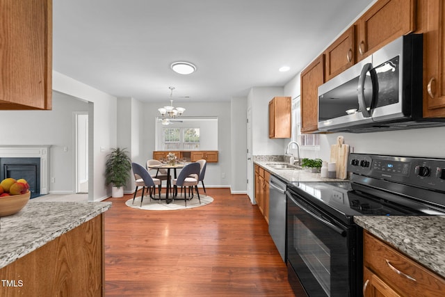 kitchen with a fireplace with flush hearth, appliances with stainless steel finishes, brown cabinets, dark wood-style flooring, and a sink