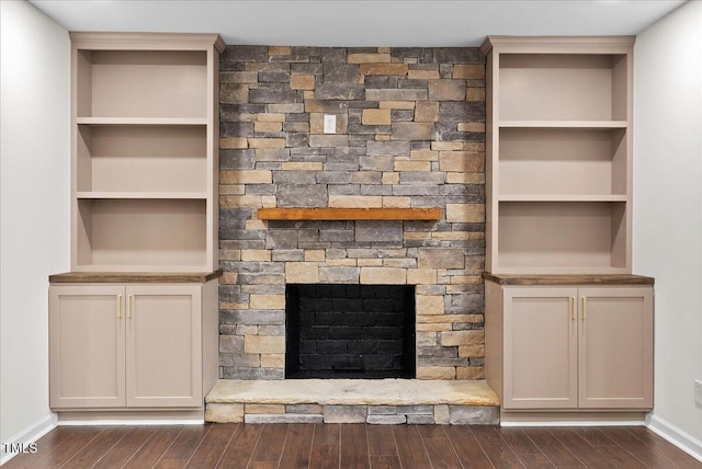 unfurnished living room with built in features, baseboards, dark wood-type flooring, and a stone fireplace