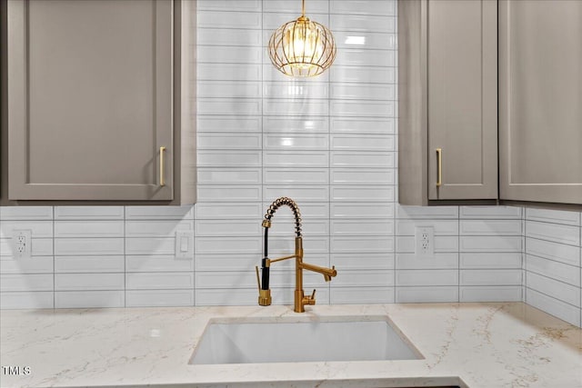 interior details featuring a sink, gray cabinets, backsplash, light stone countertops, and pendant lighting