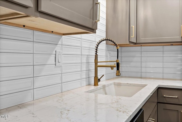 room details featuring gray cabinets, backsplash, a sink, and light stone counters