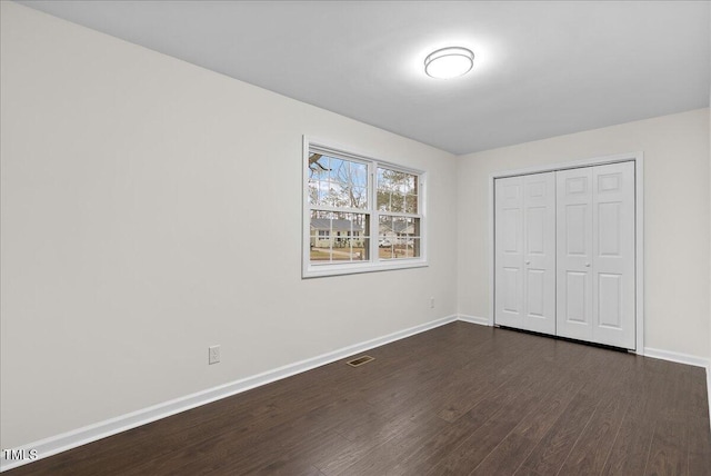 unfurnished bedroom with dark wood-style floors, a closet, visible vents, and baseboards