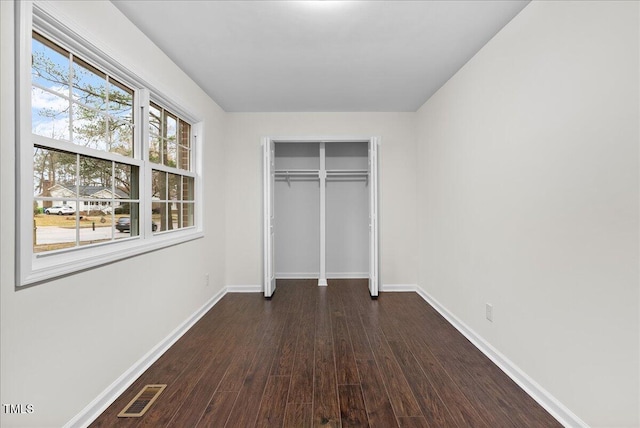 unfurnished bedroom with dark wood-style floors, baseboards, visible vents, and a closet