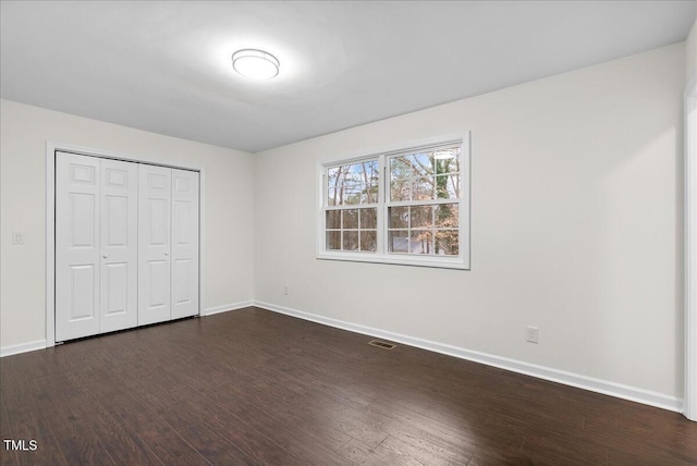 unfurnished bedroom with dark wood-style floors, visible vents, baseboards, and a closet