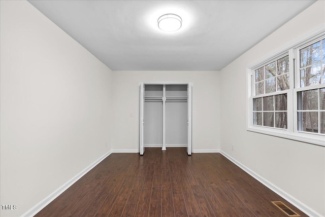 unfurnished bedroom featuring dark wood-type flooring, a closet, visible vents, and baseboards