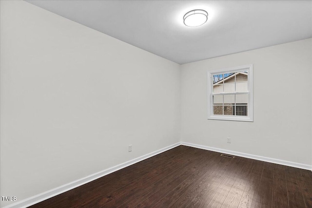 empty room featuring visible vents, dark wood finished floors, and baseboards