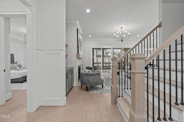 interior space featuring light wood-style flooring, stairway, an inviting chandelier, crown molding, and a fireplace