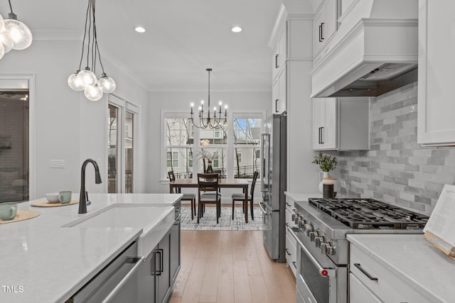 kitchen featuring premium appliances, custom range hood, crown molding, a chandelier, and a sink