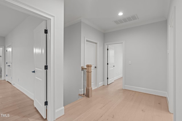 hall featuring light wood-style flooring, an upstairs landing, visible vents, baseboards, and crown molding