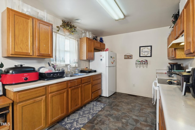 kitchen with light countertops, stone finish floor, a sink, white appliances, and under cabinet range hood