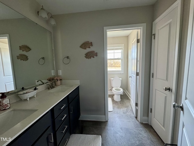 full bathroom featuring double vanity, a sink, toilet, and baseboards