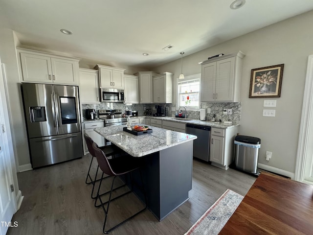 kitchen with a breakfast bar, wood finished floors, a sink, appliances with stainless steel finishes, and backsplash