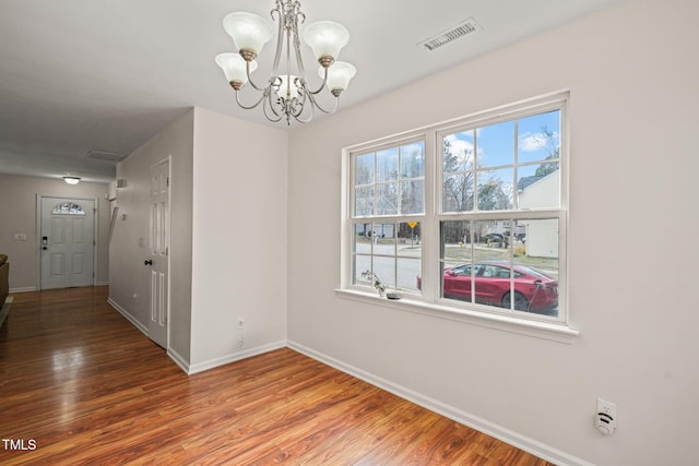 unfurnished dining area featuring a chandelier, visible vents, baseboards, and wood finished floors