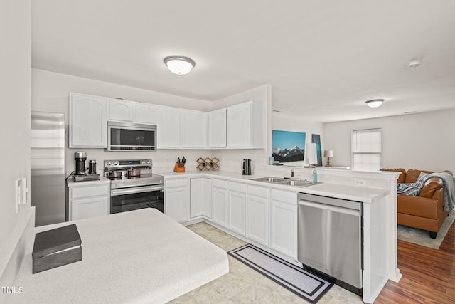 kitchen featuring stainless steel appliances, open floor plan, white cabinets, and a peninsula